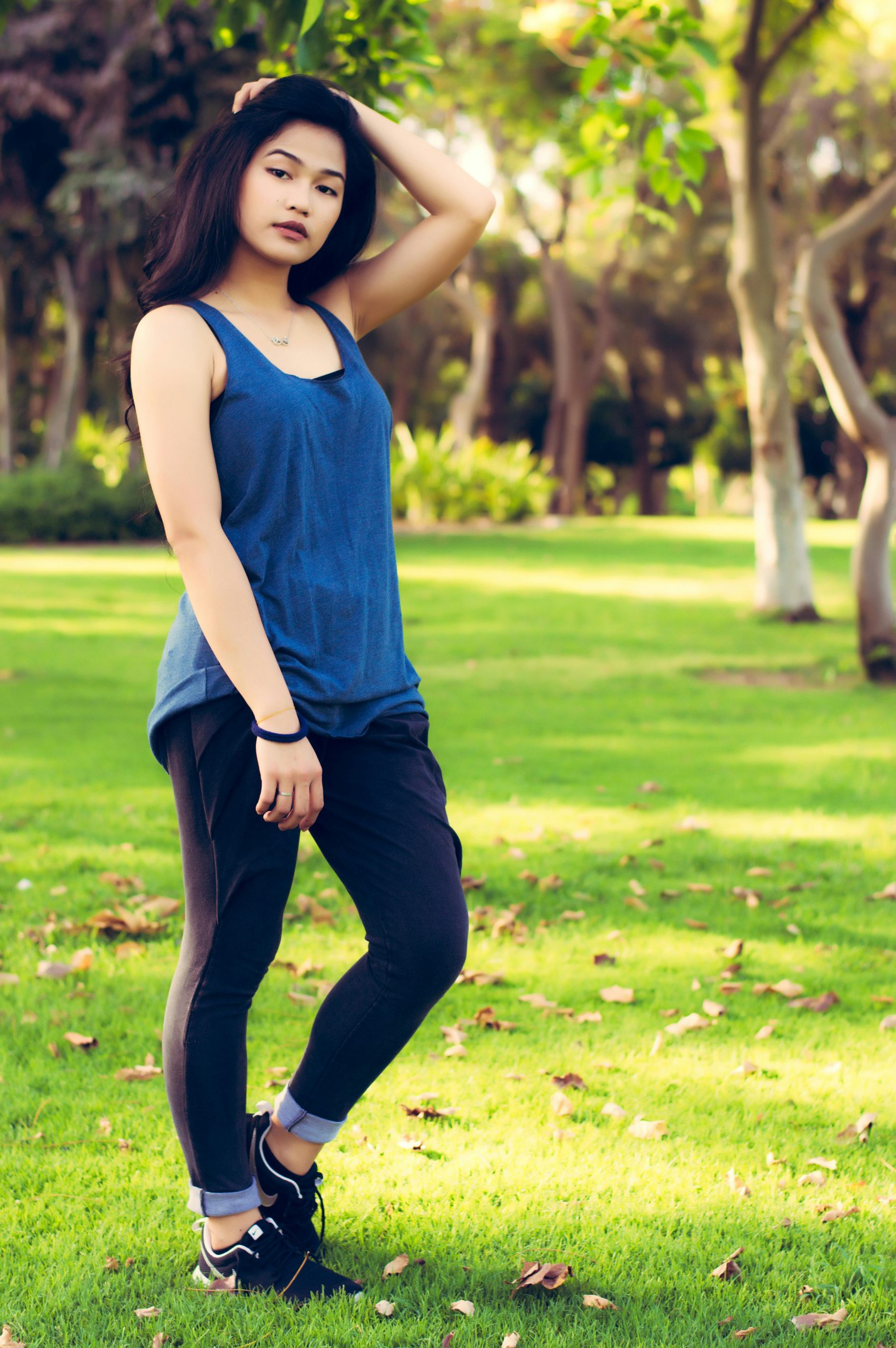 A stylish young woman stands confidently in a lush Dubai park under the sun.